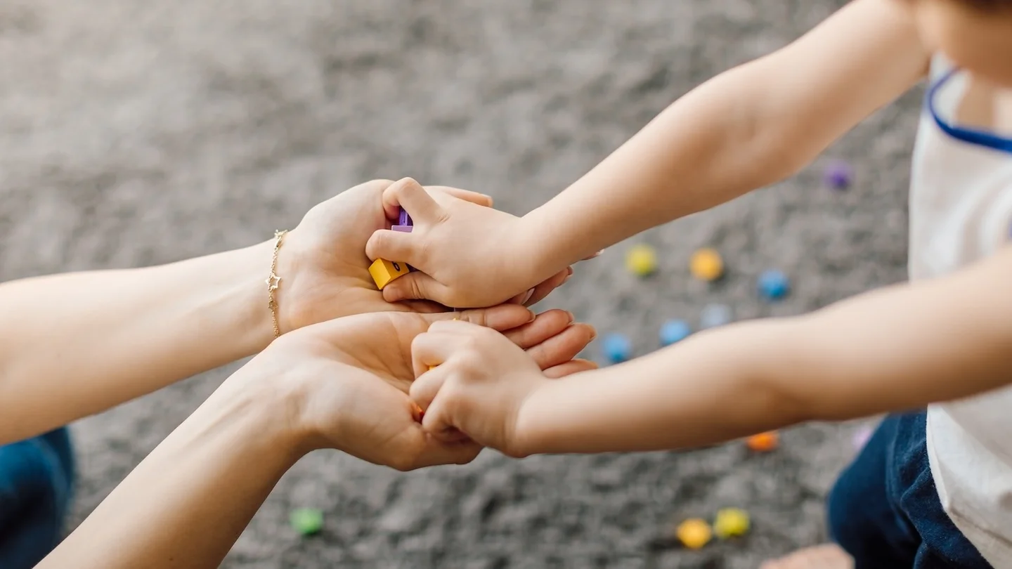 Child-like hands passing small colorful blocks to an adult