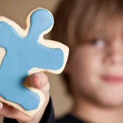 Child holds up puzzle piece cookie